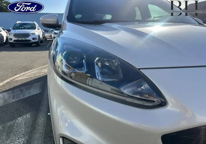 Gros plan sur le phare avant gauche d’un Ford Kuga blanc Premium Platinum sous lumière naturelle.