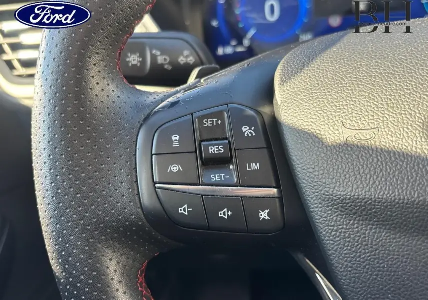 Gros plan sur le volant cuir perforé noir du Ford Kuga 2021 avec commandes multifonctions et surpiqûres rouges.