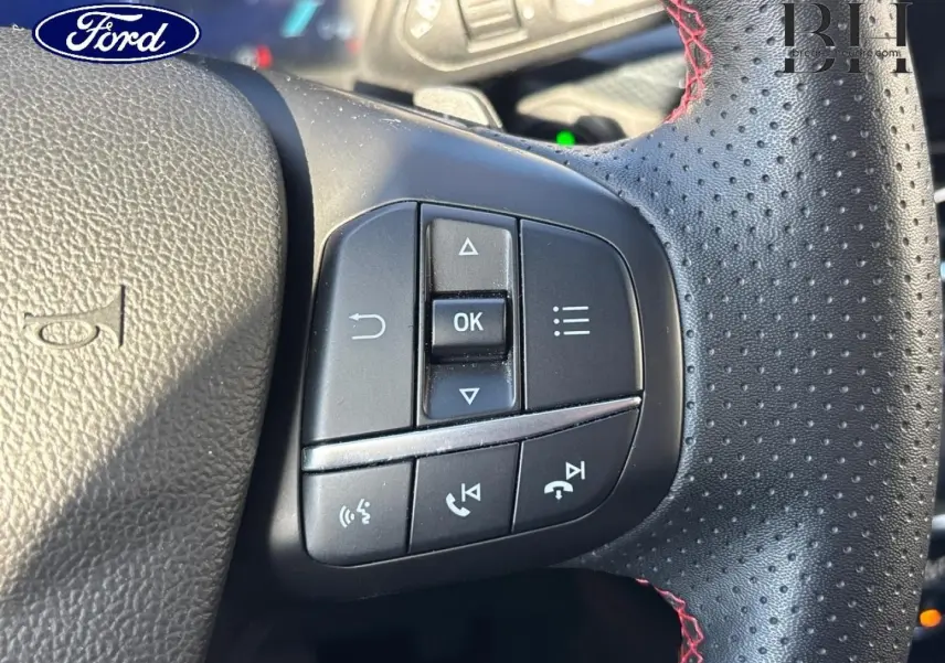 Gros plan sur les commandes multifonctions à droite du volant cuir perforé avec surpiqûres rouges du Ford Kuga blanc.