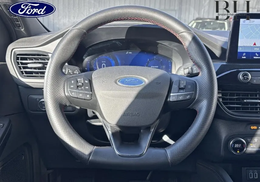 Vue intérieure frontale du volant cuir perforé du Ford Kuga 1.5 EcoBlue avec tableau de bord numérique et écran tactile.