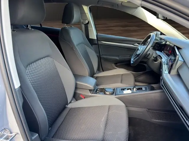 Vue intérieure côté conducteur de la Volkswagen Golf VIII gris lunaire, montrant sièges tissu et tableau de bord moderne.