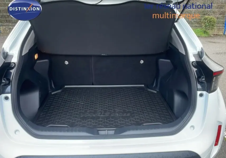 Coffre ouvert vu de l'arrière d'une Toyota Yaris Cross blanche, avec tapis de coffre noir marqué Yaris Cross.
