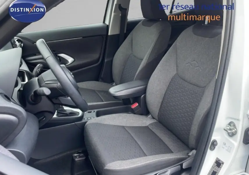 Vue intérieure côté conducteur de la Toyota Yaris Cross Hybrid blanche, sièges tissu gris et volant cuir visible.