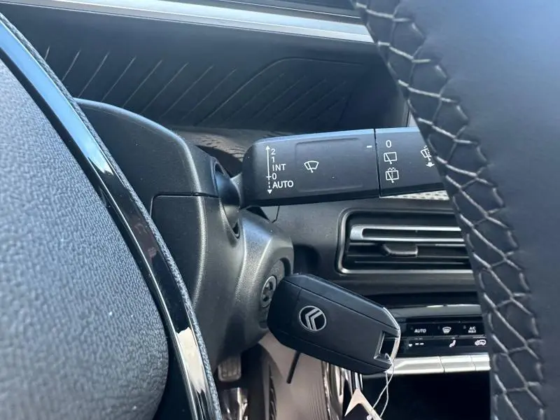 Gros plan intérieur côté gauche sur la colonne de direction avec clé Citroën insérée et commande d’essuie-glace visible.