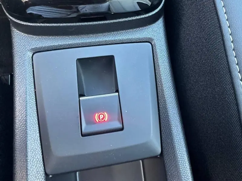 Gros plan sur le bouton de frein de stationnement électronique rouge dans l'accoudoir central du Citroën C3 Aircross gris Mercury.