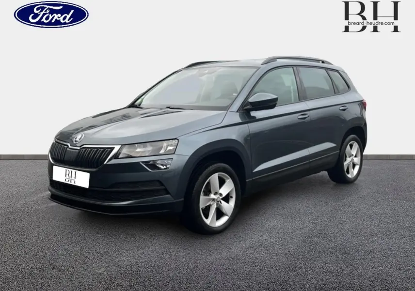 SUV Skoda Karoq gris Business vu en 3/4 avant droit, avec jantes alliage et barres de toit visibles.