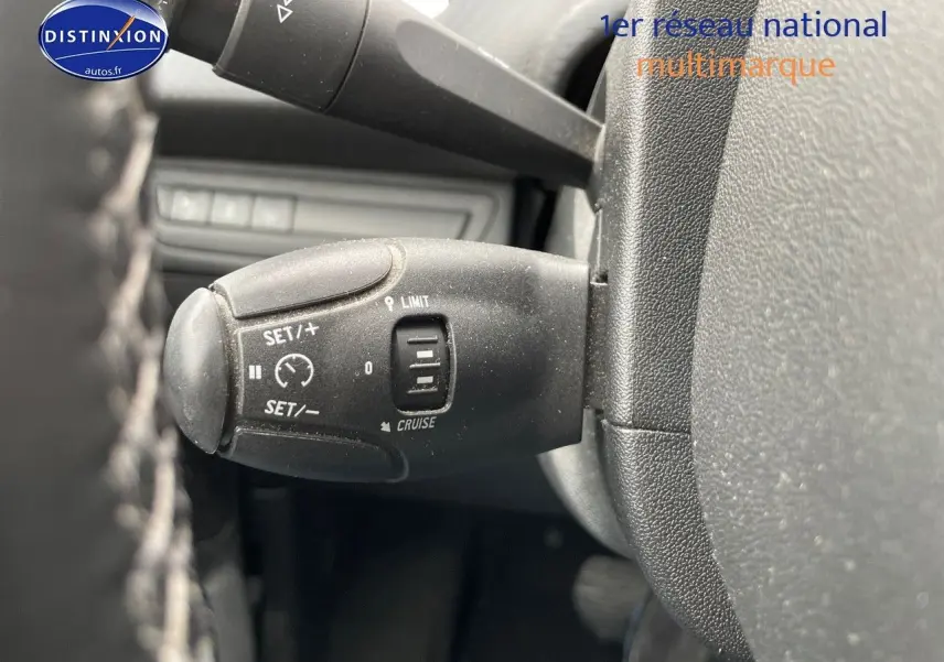 Gros plan sur la commande de régulateur de vitesse à gauche du volant d'un Peugeot 2008 blanc nacré de 2015.