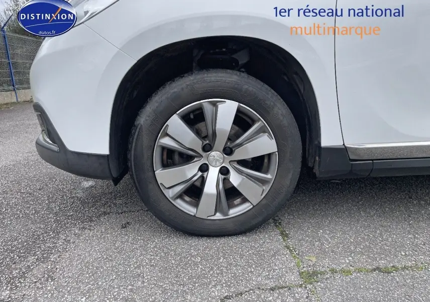 Gros plan sur la roue avant gauche d'un Peugeot 2008 blanc nacré, mettant en valeur la jante alliage et le passage de roue.