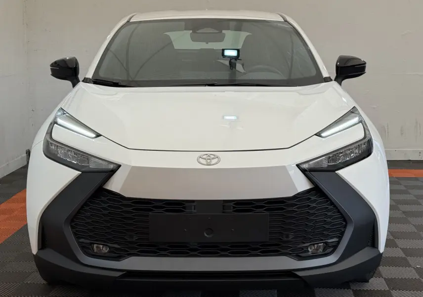 Vue frontale du Toyota C-HR 1.8 Hybride blanc avec calandre noire et phares LED fins allumés.