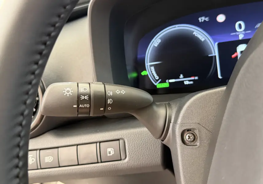 Gros plan sur la manette de phares et clignotants à gauche du volant du Toyota C-HR blanc, tableau de bord numérique visible.