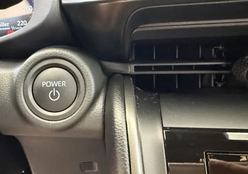 Bouton Power rond sur tableau de bord noir du Toyota C-HR 1.8 Hybride 140 Dynamic, vue intérieure rapprochée côté conducteur.