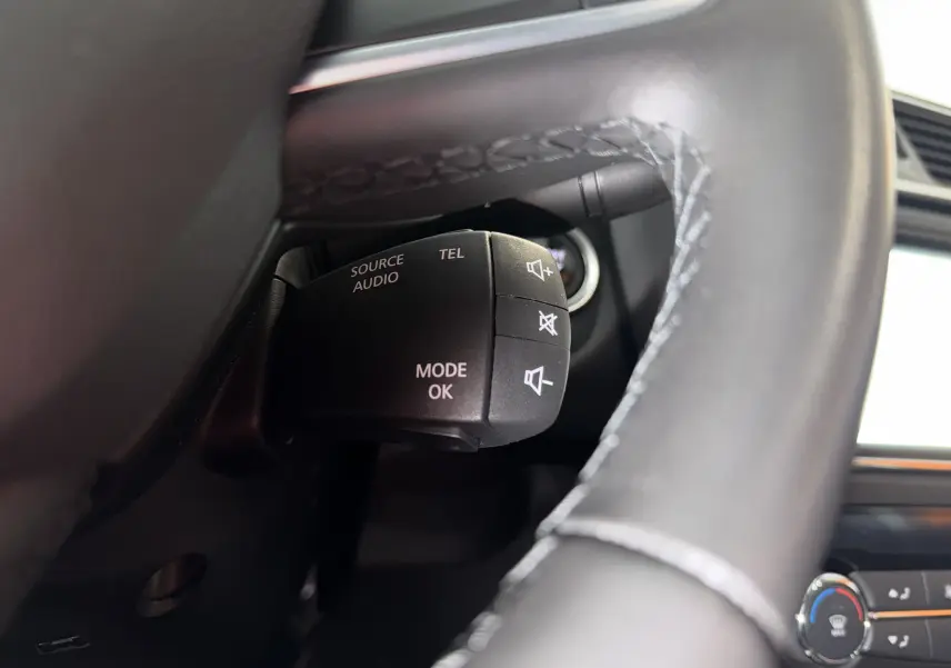 Gros plan sur la commande audio au volant noir du Renault Kadjar gris, avec boutons de volume et mode.