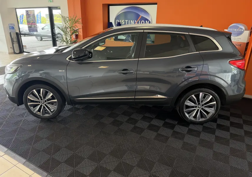Vue de profil côté gauche d'un Renault Kadjar gris 2016 en intérieur, avec jantes alliage et finitions chromées.
