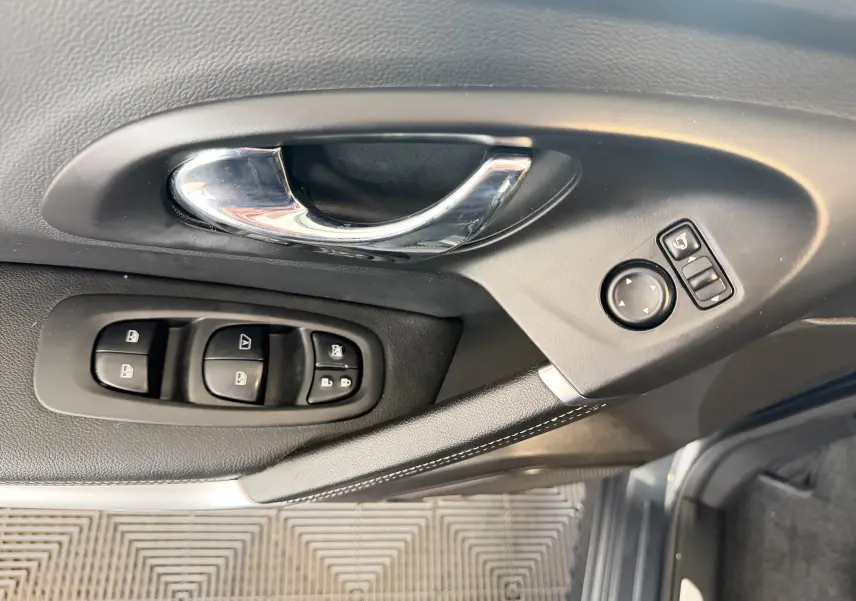 Poignée intérieure chromée et commandes électriques des vitres et rétroviseurs sur la porte côté conducteur d’un Renault Kadjar gris.