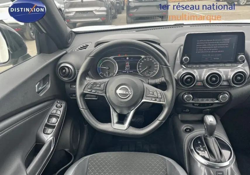Vue intérieure avant du Nissan Juke blanc 2024, volant cuir, écran tactile et commandes au volant visibles.