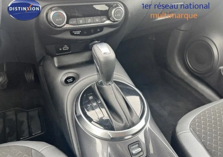 Vue rapprochée de la console centrale du Nissan Juke blanc 2024, mettant en valeur le levier de vitesse automatique et les commandes climatisation.