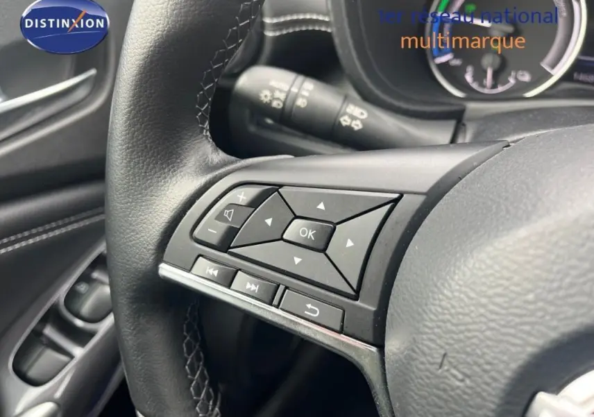 Gros plan sur les commandes multimédia au volant cuir noir du Nissan Juke blanc, version 2024, côté gauche.