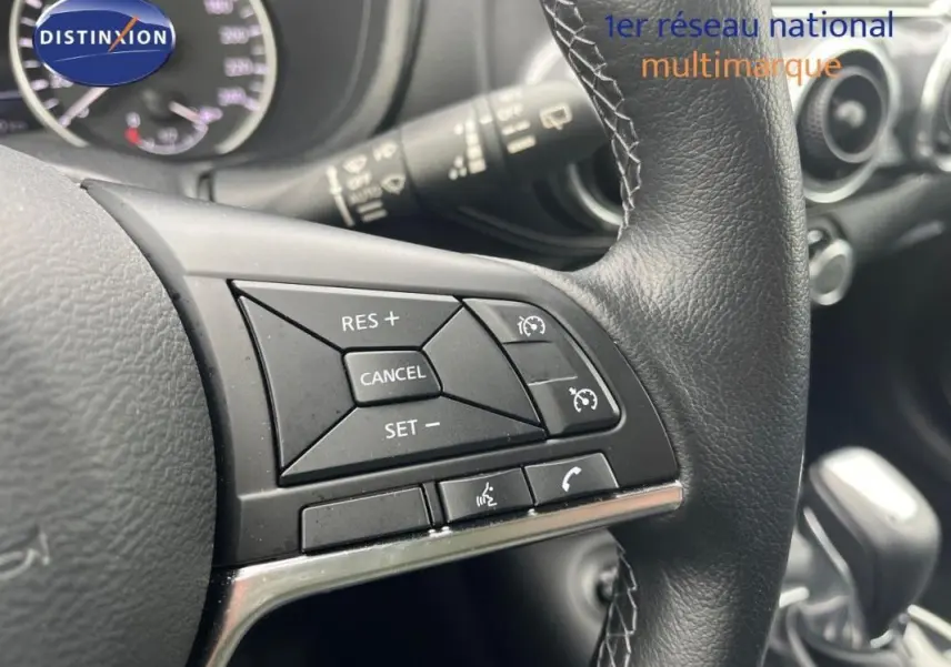 Gros plan sur les commandes du régulateur de vitesse au volant cuir noir du Nissan Juke blanc, intérieur moderne.