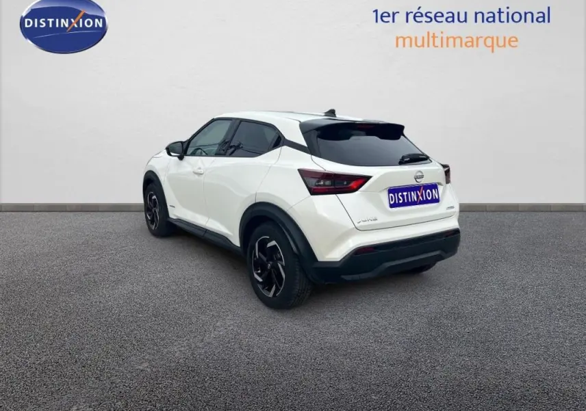Vue 3/4 arrière droite d'un Nissan Juke blanc 2024 avec jantes aluminium et toit noir contrasté.
