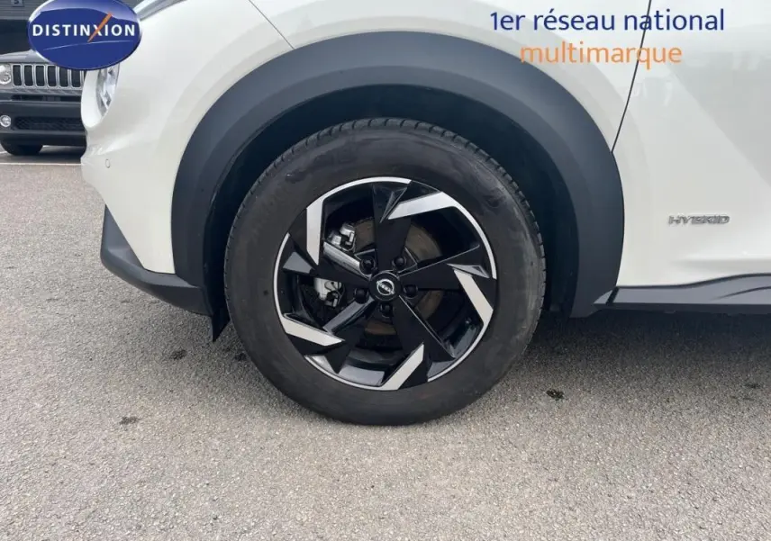 Gros plan sur la roue avant droite d’un Nissan Juke blanc 2024 avec jante aluminium noire et argentée, badge Hybrid visible.