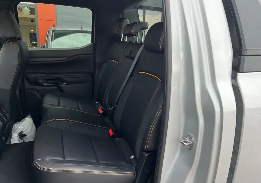 Vue latérale intérieure arrière du Ford Ranger gris iconic, sièges noirs avec surpiqûres orange et ceinture de sécurité grise.
