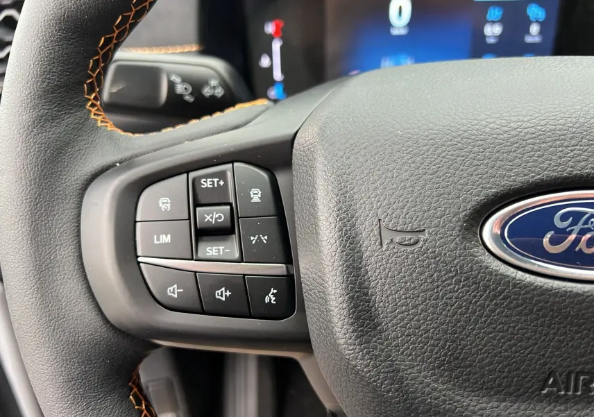 Gros plan sur le volant cuir noir du Ford Ranger 2026 avec commandes multifonctions et surpiqûres orange visibles.