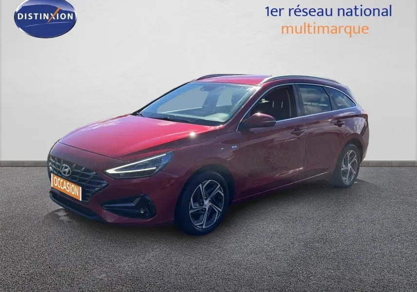 Hyundai i30 SW 2023 Sunset Red Metal vue 3/4 avant droit, avec jantes bi-ton et feux LED allumés.