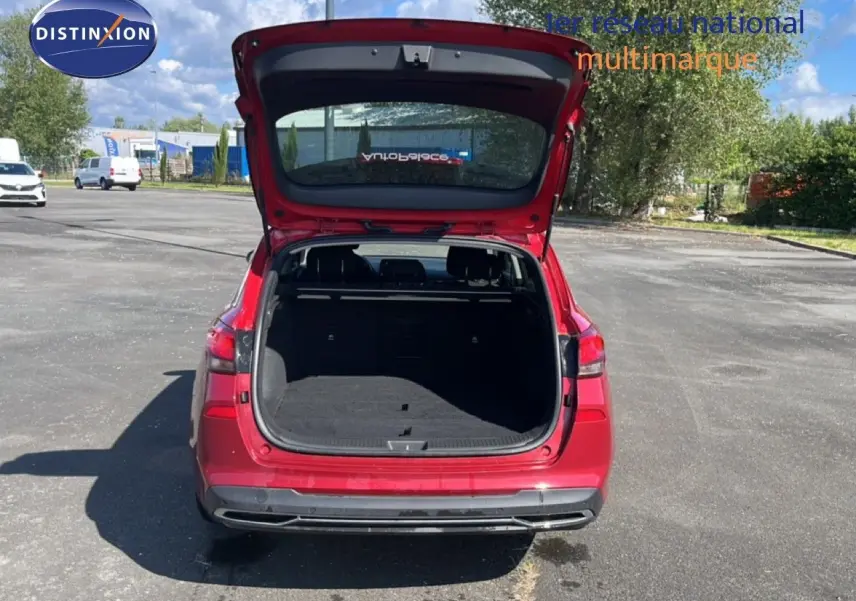 Vue arrière d’une Hyundai i30 SW 2023 en rouge Sunset Red Metal avec coffre ouvert sur un parking extérieur.