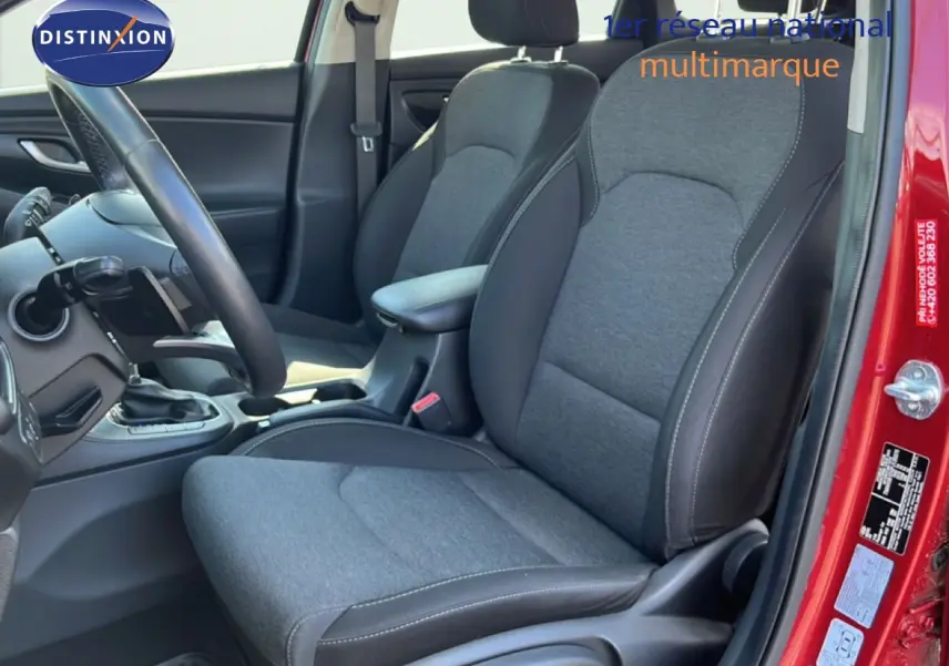 Vue intérieure côté conducteur de la Hyundai i30 SW 2023 rouge Sunset Red Metal, sièges tissu gris et cuir noir.