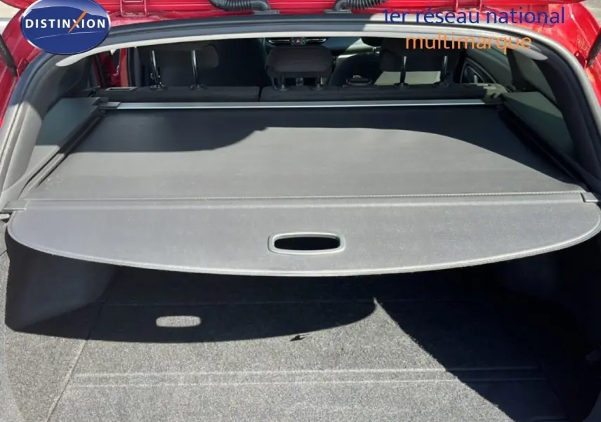 Vue arrière du coffre ouvert d'une Hyundai i30 SW 2023 rouge avec cache-bagages déployé et banquette arrière visible.