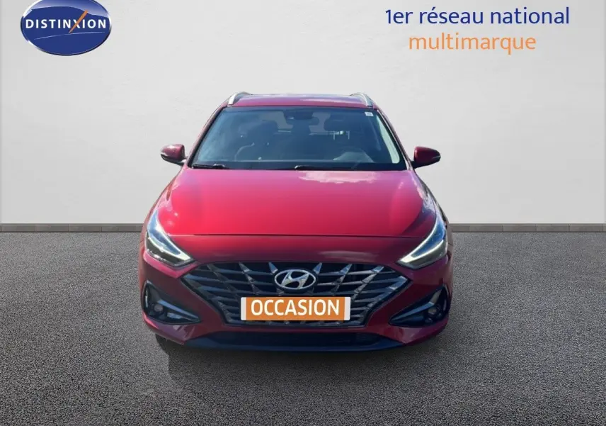 Vue frontale d'une Hyundai i30 SW 2023 rouge Sunset Red Metal avec calandre distinctive et phares LED allumés.