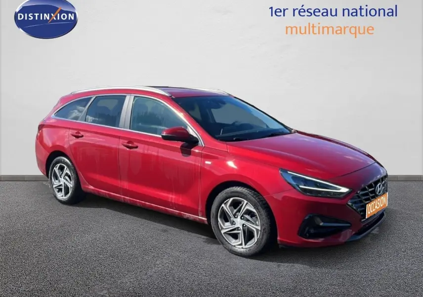 Hyundai i30 SW 2023 rouge Sunset Red Metal vue 3/4 avant droit avec jantes alliage biton et feux LED allumés.