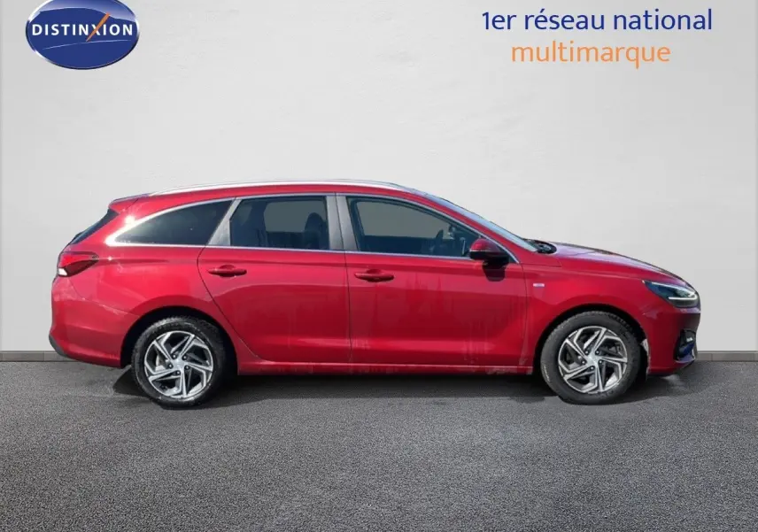 Profil droit d'une Hyundai i30 SW 2023 rouge Sunset Red Metal avec jantes alliage et toit ouvrant visible.