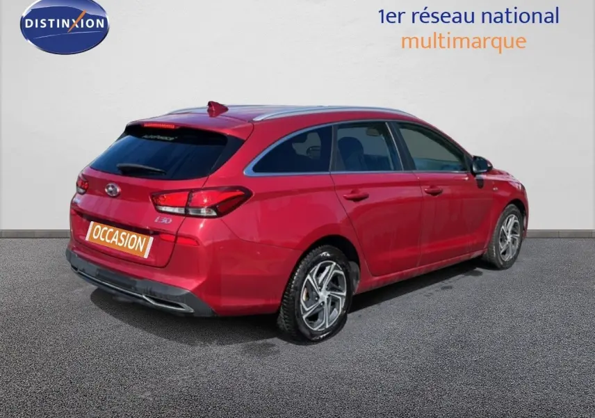 Vue 3/4 arrière droite d'une Hyundai i30 SW 2023 rouge Sunset Red Metal avec jantes bi-ton et feux LED.