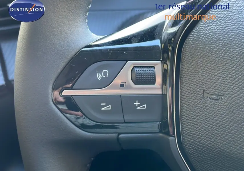 Gros plan sur les commandes de volume et téléphone au volant d’une Peugeot 208 noir perla metal, version hybride 2026.
