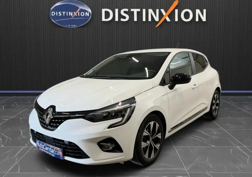 Renault Clio V blanche vue 3/4 avant droit, jantes bi-ton et rétroviseurs noirs, stationnée en intérieur showroom.