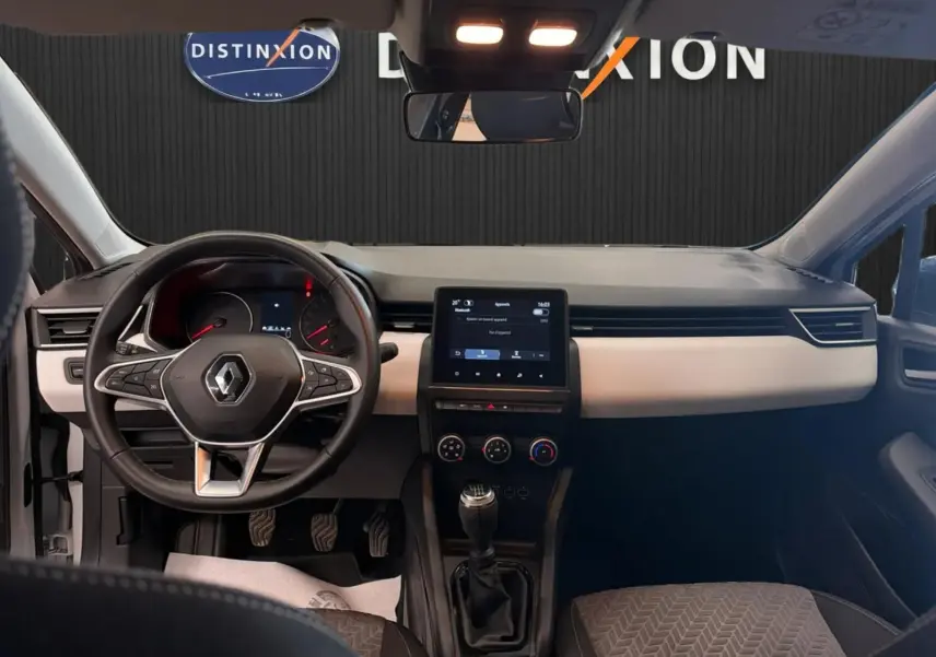 Vue intérieure avant de la Renault Clio V blanche, tableau de bord gris clair avec écran tactile et volant multifonction.