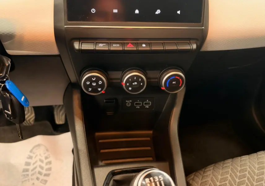 Vue rapprochée du tableau de bord et de la console centrale de la Renault Clio V blanche, avec commandes de climatisation et levier de vitesses manuel.