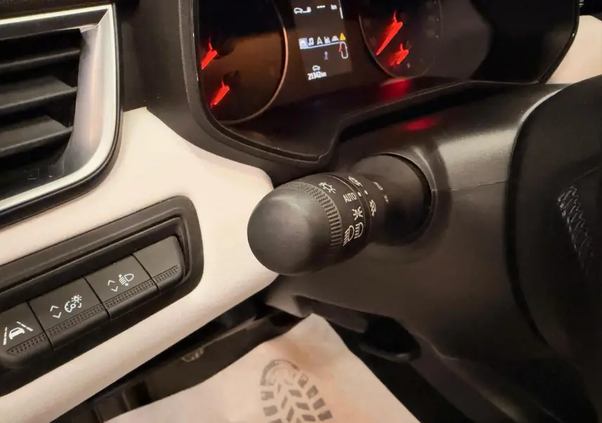 Détail du commodo d’éclairage et tableau de bord partiel de la Renault Clio V blanche, intérieur gris.