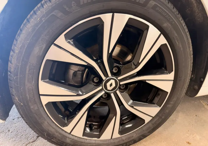 Gros plan sur la jante alliage bicolore noire et argentée d'une Renault Clio V blanche, roue avant droite.
