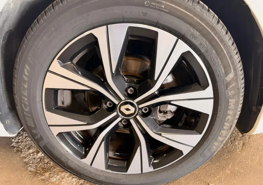 Gros plan sur la jante alliage bicolore noire et argentée avec logo Renault, pneu Michelin, sur Clio V blanche.