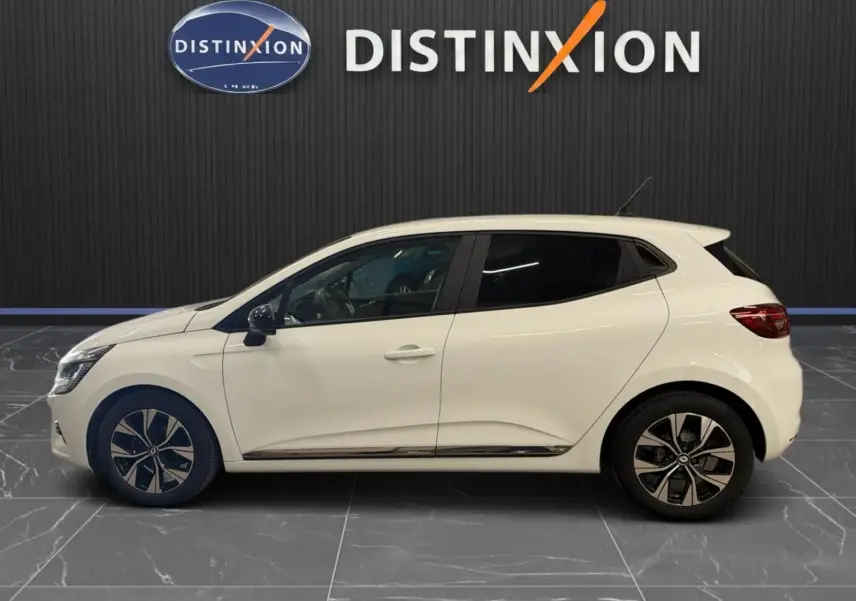 Profil côté gauche d'une Renault Clio V blanche 5 portes avec jantes bi-ton et vitres teintées, en intérieur showroom.