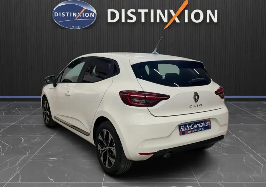Vue 3/4 arrière droite d'une Renault Clio V blanche, avec jantes bi-ton et vitres teintées, en intérieur showroom.