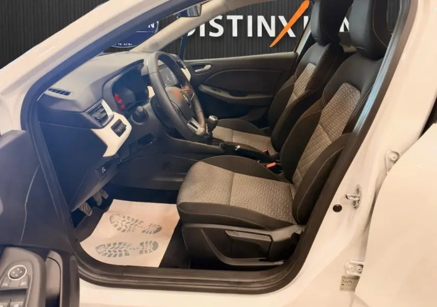 Intérieur de la Renault Clio V blanc vue côté gauche, sièges bi-ton gris et noir avec volant et tableau de bord visibles.