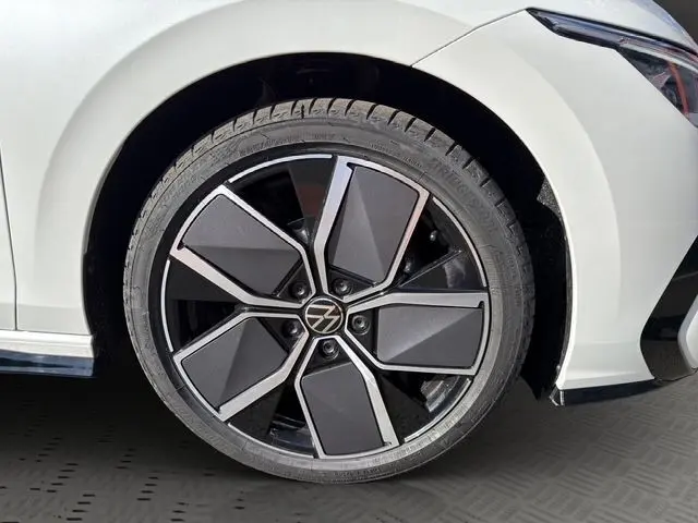 Gros plan sur la roue avant droite noire et argentée d'une Volkswagen Golf blanche 2025 avec partie avant visible.
