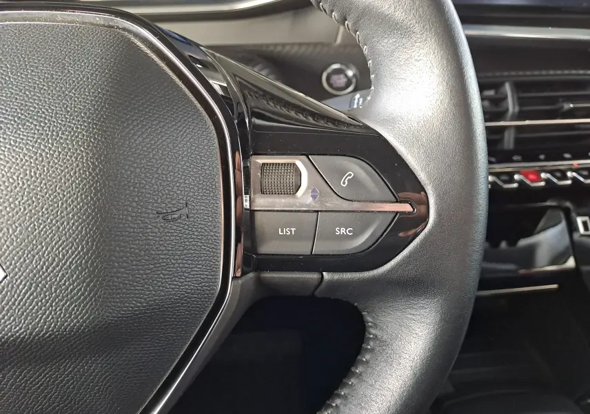 Gros plan sur le côté droit du volant en cuir noir du Peugeot 2008 1.2 PureTech 100 Allure, avec commandes intégrées.