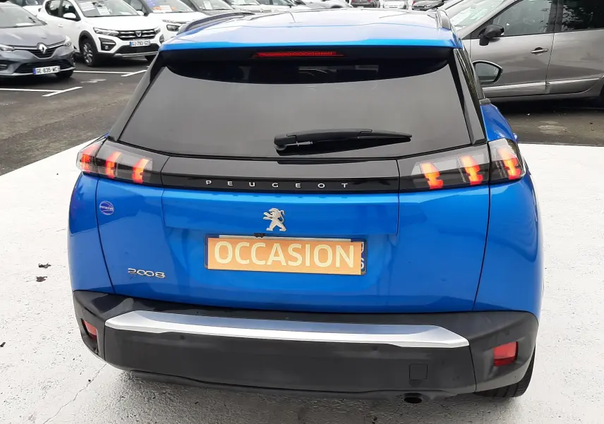 Vue arrière d'un Peugeot 2008 bleu Vertigo avec feux arrière à griffes et plaque "OCCASION" visible sur un parking.