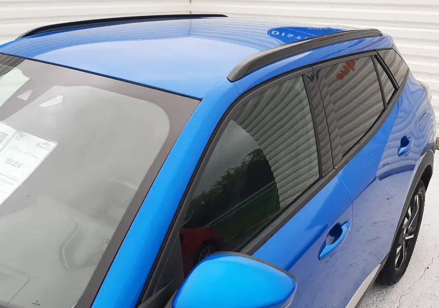 Vue 3/4 avant droit d'un Peugeot 2008 bleu Vertigo avec barres de toit noires et vitres teintées.