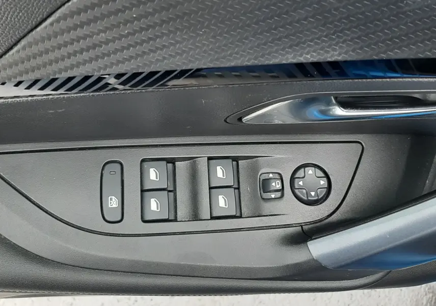 Gros plan sur la commande des vitres et rétroviseurs côté conducteur d'une Peugeot 2008 bleu Vertigo, finition intérieure noire.