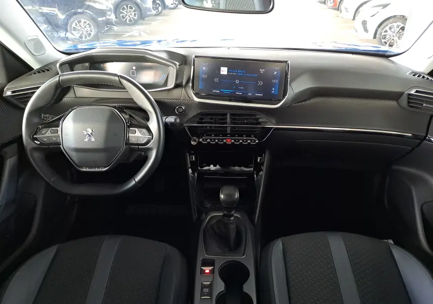 Vue intérieure frontale du tableau de bord et volant noir du Peugeot 2008 bleu Vertigo avec écran tactile et levier de vitesses manuel.